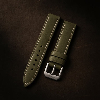 Wichtelmänner Olive Green full-grain leather watch strap with contrast stitching, flat lay on a leather workbench